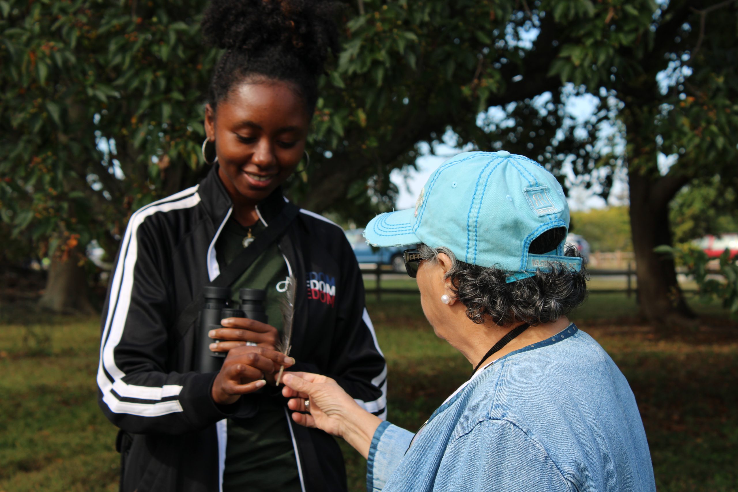 Two women exchange a feather in the outdoors.